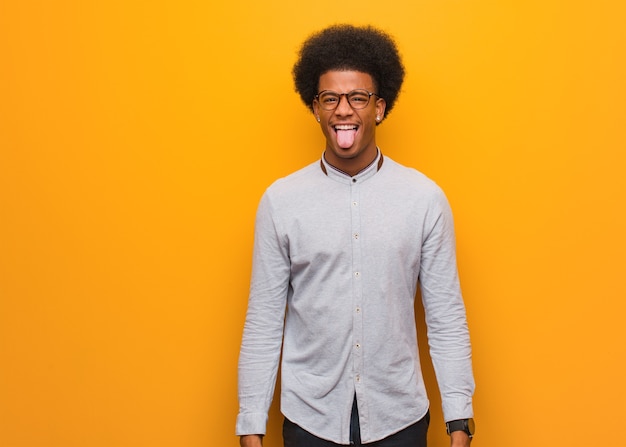Jonge Afro-Amerikaanse man over een oranje muur funnny en vriendelijke tonende tong