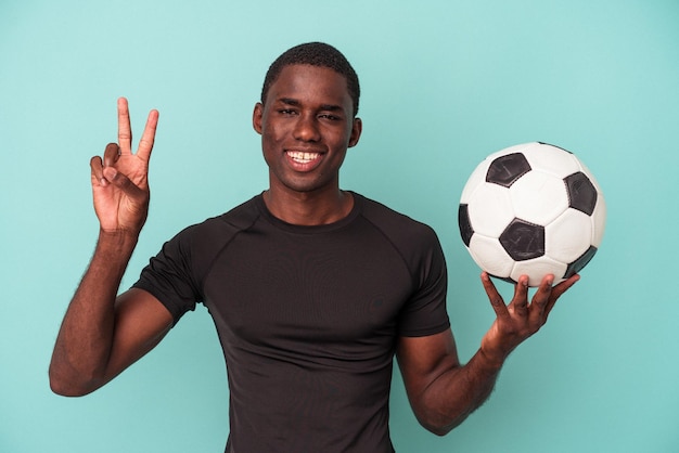 Jonge Afro-Amerikaanse man voetballen geïsoleerd op blauwe achtergrond met nummer twee met vingers