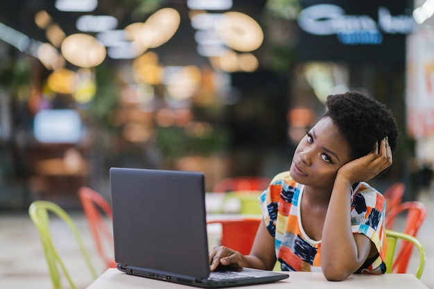 Jonge Afro-Amerikaanse meisjeszitting bij koffielijst met laptop en het bekijken het scherm. Donkere huid freelancer concept.