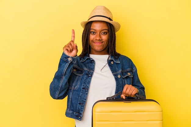 Jonge Afro-Amerikaanse reiziger vrouw met koffer geïsoleerd op gele achtergrond met nummer één met vinger.