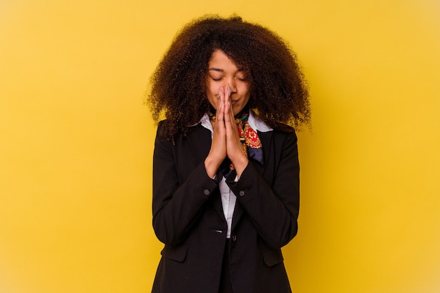 Jonge Afro-Amerikaanse stewardess geïsoleerd op geel hand in hand bidden in de buurt van mond, voelt zich zelfverzekerd.