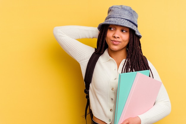 Jonge Afro-Amerikaanse student vrouw geïsoleerd op geel achterkant van het hoofd aanraken, denken en een keuze maken.