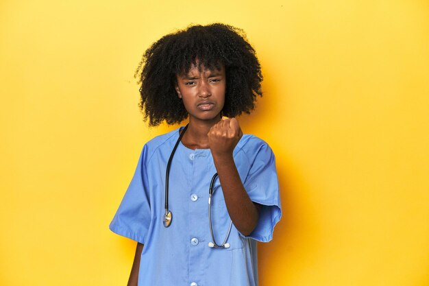 Foto jonge afro-amerikaanse verpleegster in de studio met gele achtergrond die de vuist naar de camera toont