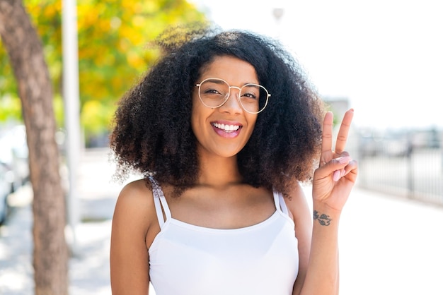 Jonge Afro-Amerikaanse vrouw buiten met een bril en een OK-teken.