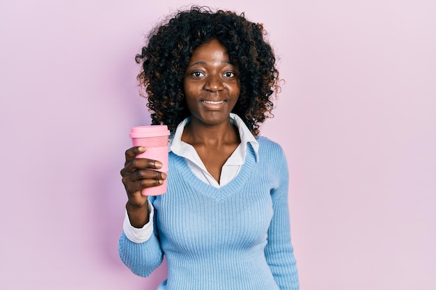 Jonge afro-amerikaanse vrouw die afhaalkoffie drinkt, ziet er positief en gelukkig uit en glimlacht met een zelfverzekerde glimlach die tanden laat zien