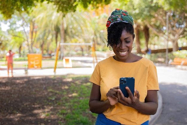Jonge afro-amerikaanse vrouw die lacht terwijl ze een bericht typt op de mobiele telefoon