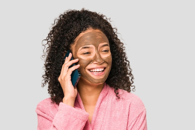 Jonge afro-amerikaanse vrouw die telefonisch praat terwijl ze een geïsoleerd gezichtsmasker aanbrengt