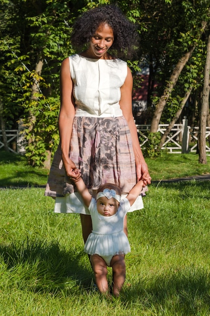 Jonge Afro-Amerikaanse vrouw en haar dochter glimlachend wandelen in zomer park.