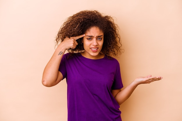 Jonge afro-amerikaanse vrouw geïsoleerd op beige achtergrond met een teleurstelling gebaar met wijsvinger.
