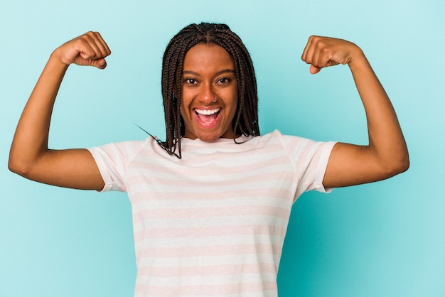 Jonge afro-amerikaanse vrouw geïsoleerd op blauwe achtergrond met krachtgebaar met armen, symbool van vrouwelijke kracht