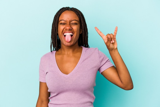 Jonge afro-amerikaanse vrouw geïsoleerd op blauwe achtergrond met rock gebaar met vingers