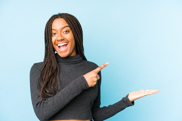 Jonge Afro-Amerikaanse vrouw geïsoleerd op blauwe achtergrond opgewonden met een kopie ruimte op palm.