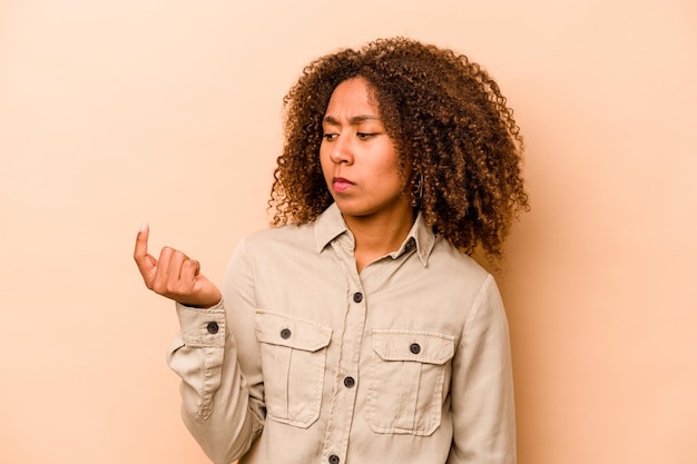 Jonge afro-amerikaanse vrouw geïsoleerd op een beige achtergrond die met de vinger naar je wijst alsof uitnodigend dichterbij komt