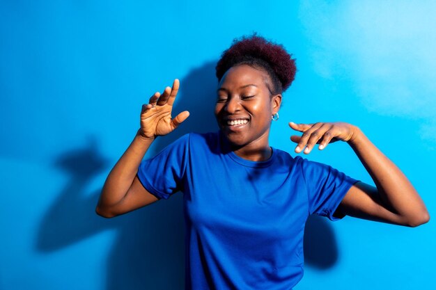 Jonge afro-amerikaanse vrouw geïsoleerd op een blauwe achtergrond glimlachend en dansende studio shoot