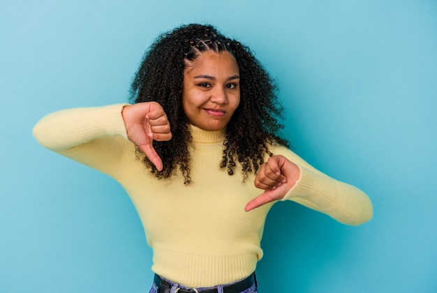 Jonge Afro-Amerikaanse vrouw geïsoleerd op een blauwe achtergrond met duim omlaag, teleurstelling concept.