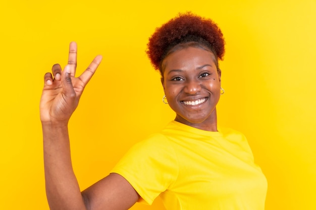 Jonge afro-amerikaanse vrouw geïsoleerd op een gele achtergrond glimlachend met de studio-shoot van het overwinningsgebaar