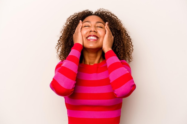 Foto jonge afro-amerikaanse vrouw geïsoleerd op een witte achtergrond lacht vreugdevol handen op het hoofd houden geluk concept