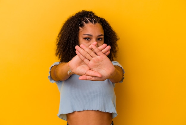 Jonge afro-amerikaanse vrouw geïsoleerd op gele achtergrond die een ontkenningsgebaar doet