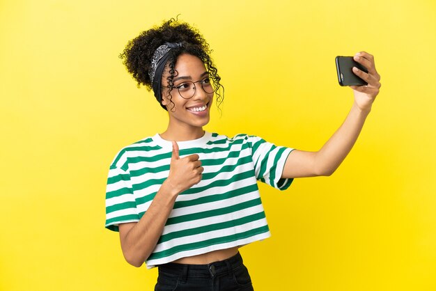 Jonge afro-amerikaanse vrouw geïsoleerd op gele achtergrond die een selfie maakt met mobiele telefoon