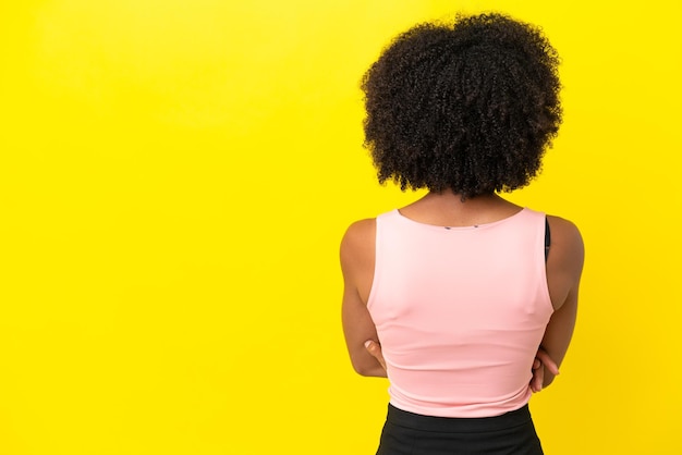 Jonge Afro-Amerikaanse vrouw geïsoleerd op gele achtergrond in achterpositie
