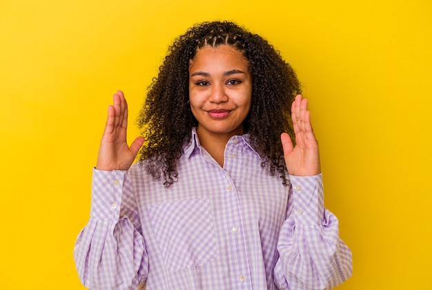 Jonge afro-amerikaanse vrouw geïsoleerd op gele achtergrond met iets kleins met wijsvingers, glimlachend en zelfverzekerd.