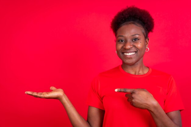 Jonge Afro-Amerikaanse vrouw geïsoleerd op rode achtergrond glimlachend en wijzend studio shoot kopie ruimte