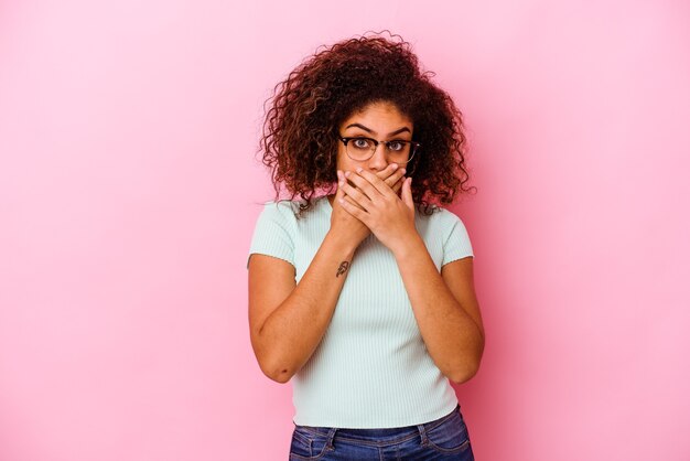 Jonge afro-amerikaanse vrouw geïsoleerd op roze achtergrond die mond bedekt met handen die bezorgd kijken.