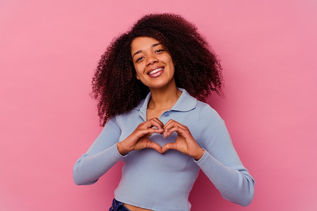 Jonge Afro-Amerikaanse vrouw geïsoleerd op roze achtergrond glimlachend en met een hartvorm met handen.