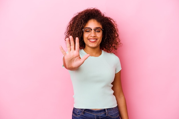 Jonge Afro-Amerikaanse vrouw geïsoleerd op roze achtergrond glimlachend vrolijk weergegeven: nummer vijf met vingers.