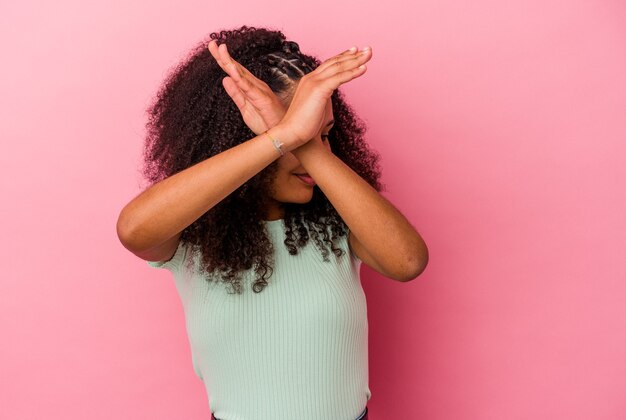 Jonge Afro-Amerikaanse vrouw geïsoleerd op roze achtergrond houden twee armen gekruist, ontkenning concept.