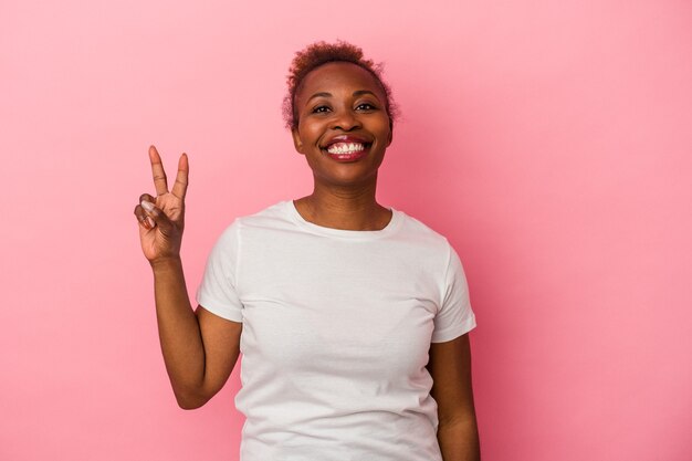 Jonge Afro-Amerikaanse vrouw geïsoleerd op roze achtergrond overwinning teken tonen en breed glimlachen.