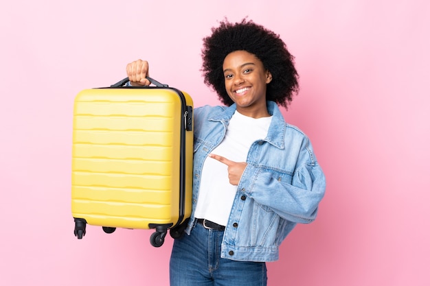 Jonge Afro-Amerikaanse vrouw geïsoleerd op roze in vakantie met reiskoffer