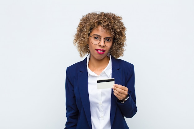 Jonge Afro-Amerikaanse vrouw gevoel verbaasd en verward, met een stomme, verbijsterde uitdrukking op zoek naar iets onverwachts met een creditcard