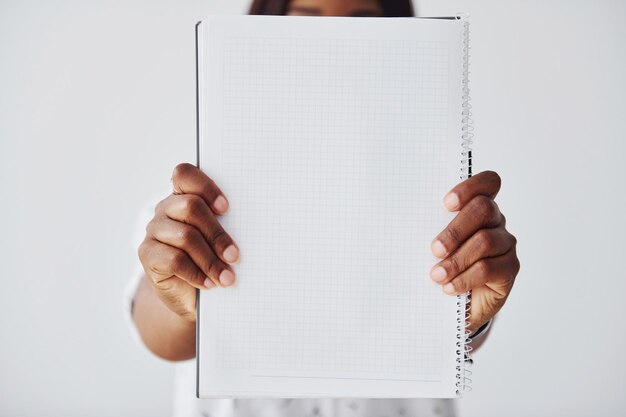 Jonge afro-amerikaanse vrouw in formele kleding die staat met notitieblok en leeg papier in handen binnenshuis