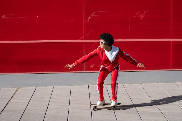 Jonge Afro-Amerikaanse vrouw in sportkleding en een skateboard op een rood gekleurde achtergrond