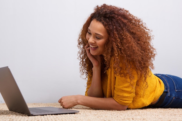 Jonge Afro-Amerikaanse vrouw ligt op de vloer en kijkt naar het laptop scherm