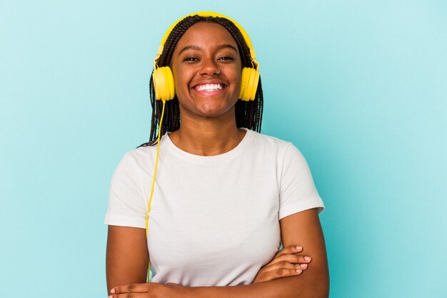 Jonge Afro-Amerikaanse vrouw luisteren naar muziek geïsoleerd op blauwe achtergrond lachen en plezier hebben.