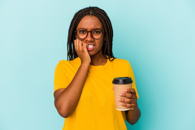 Jonge Afro-Amerikaanse vrouw met een afhaalkoffie geïsoleerd op blauwe achtergrond bijtende vingernagels, nerveus en erg angstig.
