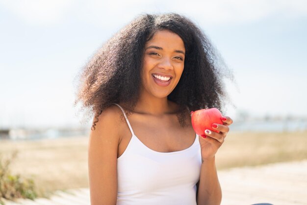 Jonge Afro-Amerikaanse vrouw met een appel buiten die veel glimlacht