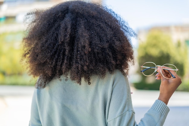 Jonge Afro-Amerikaanse vrouw met een bril buiten in de achterpositie