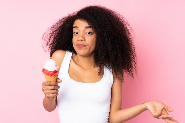 Jonge Afro-Amerikaanse vrouw met een cornet-ijs op roze muur twijfels gebaar maken terwijl het opheffen van de schouders