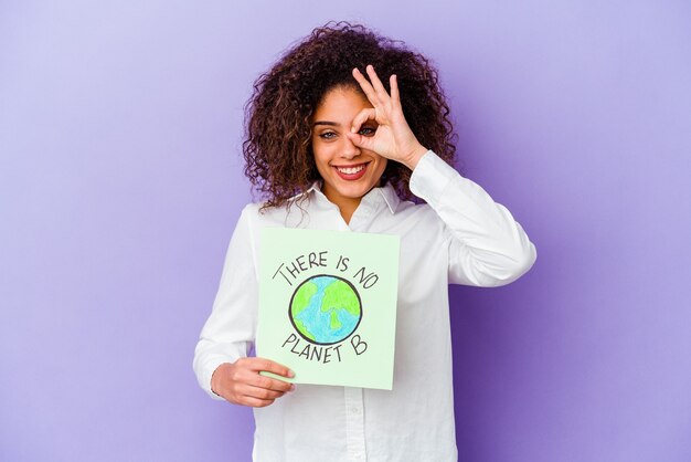 Jonge Afro-Amerikaanse vrouw met een Er is geen planeet B-plakkaat geïsoleerd opgewonden houden ok gebaar op oog.