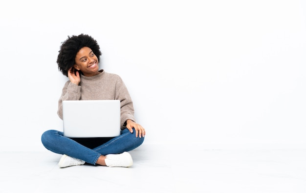 Jonge afro-amerikaanse vrouw met een laptop zittend op de vloer denken een idee