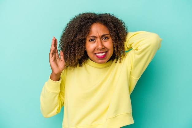 Jonge Afro-Amerikaanse vrouw met krullend haar geïsoleerd op blauwe achtergrond schreeuwen van woede.