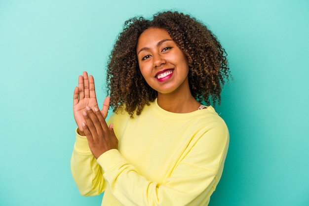 Jonge afro-amerikaanse vrouw met krullend haar geïsoleerd op blauwe achtergrond voelt zich energiek en comfortabel, wrijft zelfverzekerd over de handen.