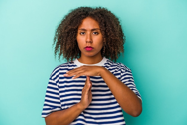 Jonge Afro-Amerikaanse vrouw met krullend haar geïsoleerd op een blauwe achtergrond met een time-outgebaar.