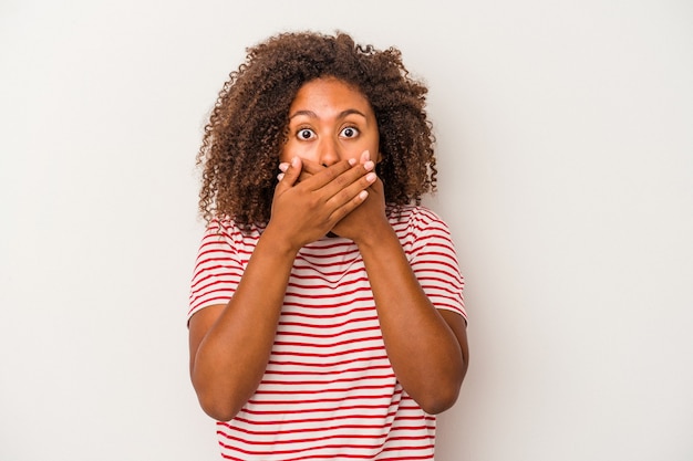 Jonge afro-amerikaanse vrouw met krullend haar geïsoleerd op een witte achtergrond die de mond bedekt met handen die bezorgd kijken.