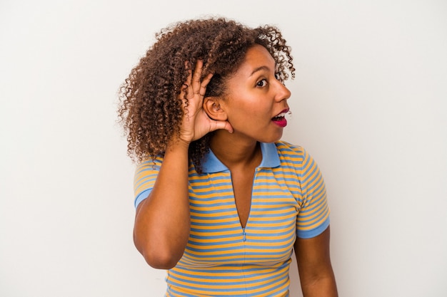 Jonge Afro-Amerikaanse vrouw met krullend haar geïsoleerd op een witte achtergrond probeert te luisteren naar een roddel.