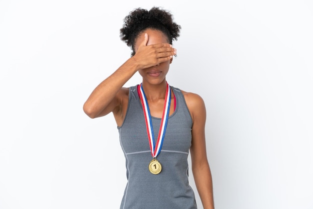 Jonge Afro-Amerikaanse vrouw met medailles geïsoleerd op een witte achtergrond die ogen bedekt door handen. Wil je iets niet zien