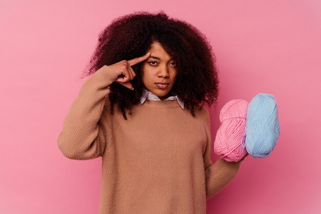 Jonge afro-amerikaanse vrouw met naaigaren geïsoleerd op roze wijzende tempel met vinger, denkend, gericht op een taak.